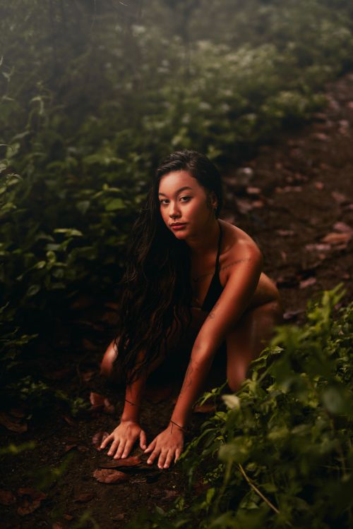 Free A woman crouching on a forest path surrounded by lush greenery, creating a serene and natural atmosphere. Stock Photo