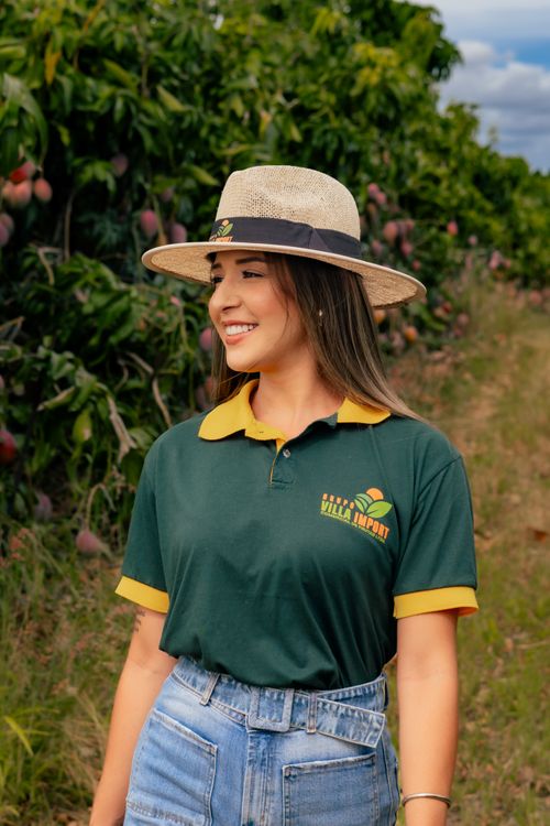 Free A woman smiles while standing in a lush mango orchard, wearing a wide-brimmed hat. Stock Photo