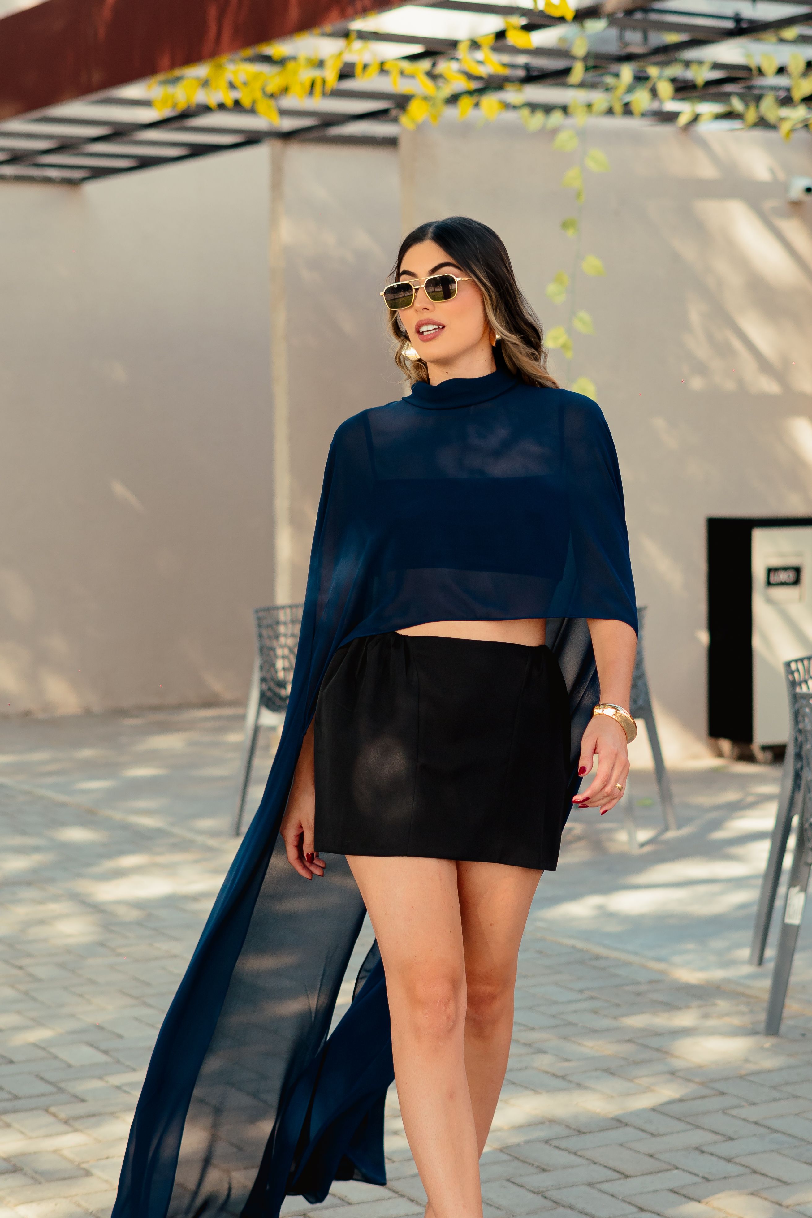 Mulher elegante de óculos escuros e roupa chique posando ao ar livre.