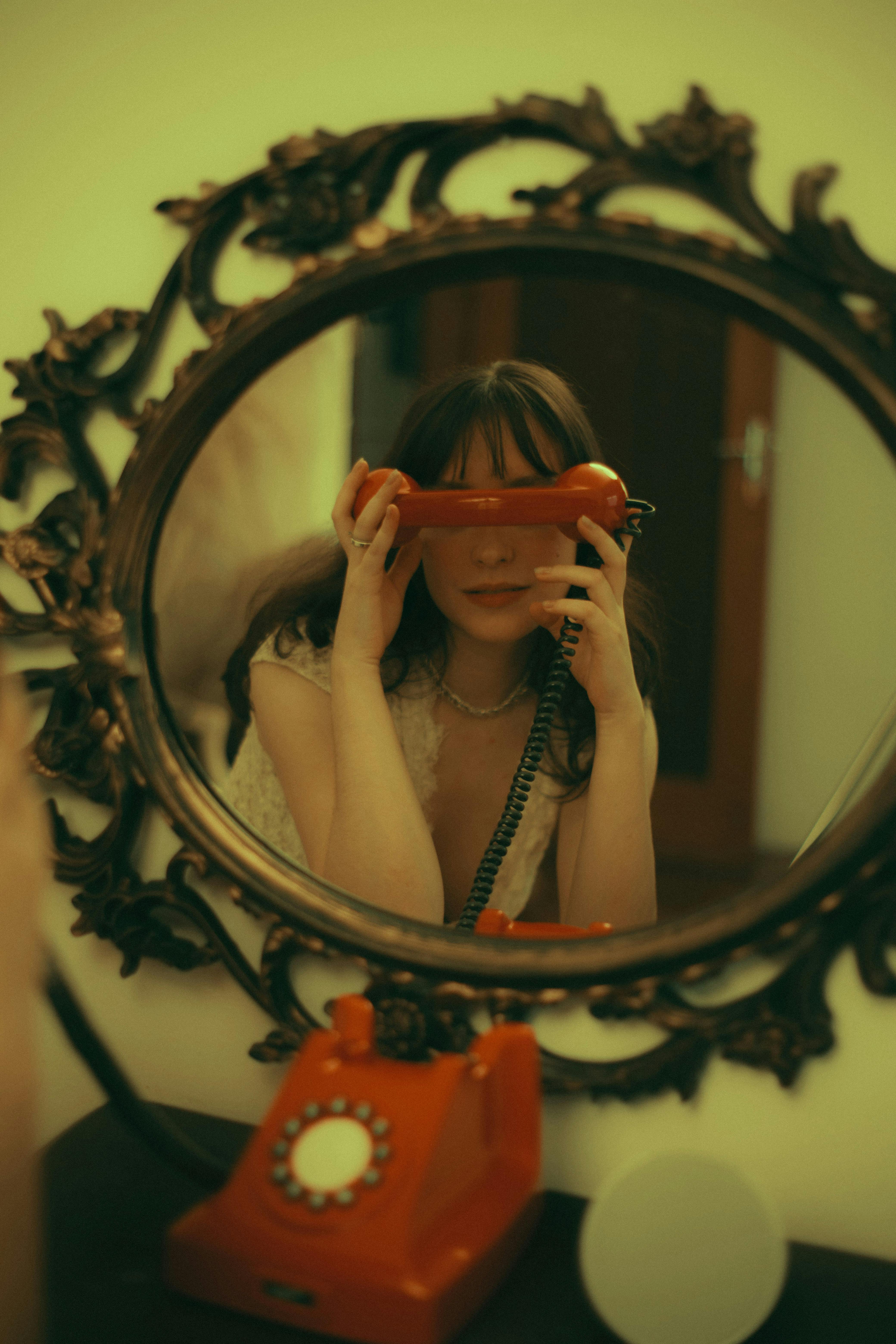 Woman holds a retro red telephone in front of an ornate mirror, creating a vintage vibe.