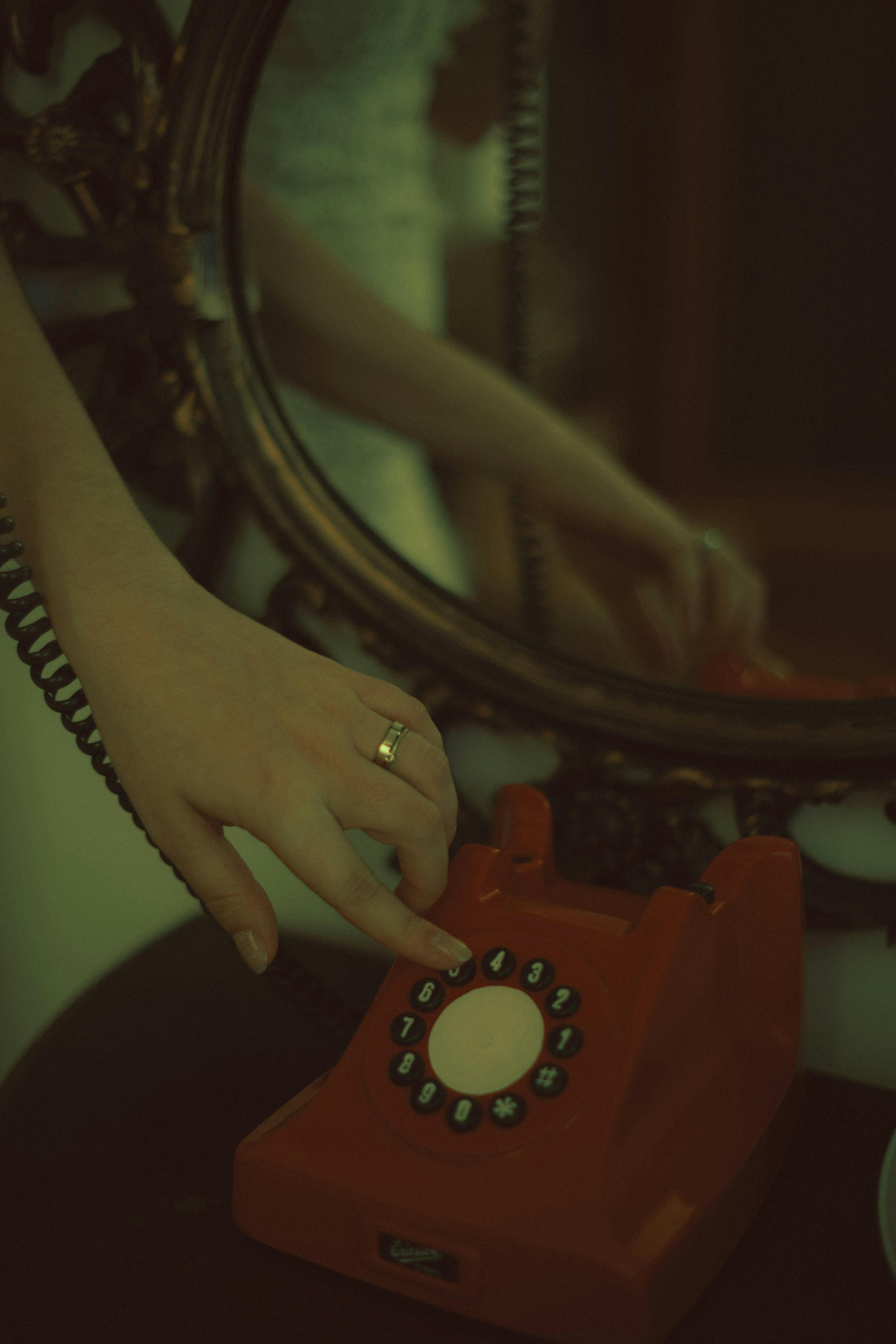 Kostnadsfria En hand som ringer en vintage röd roterande telefon med en reflektion i en dekorativ spegel. Stock foto