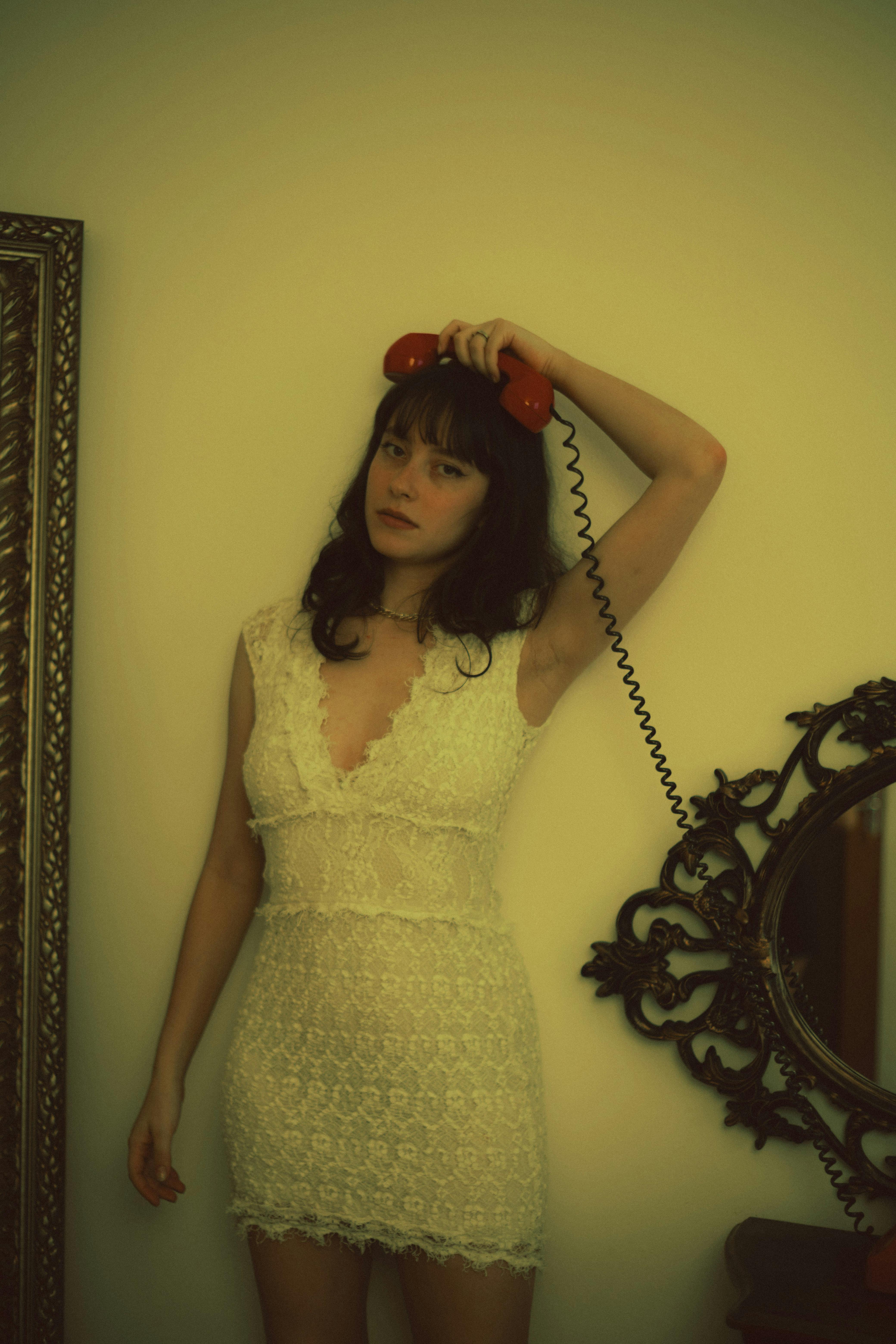 A vintage-style portrait of a woman in a lace dress holding a red rotary phone.