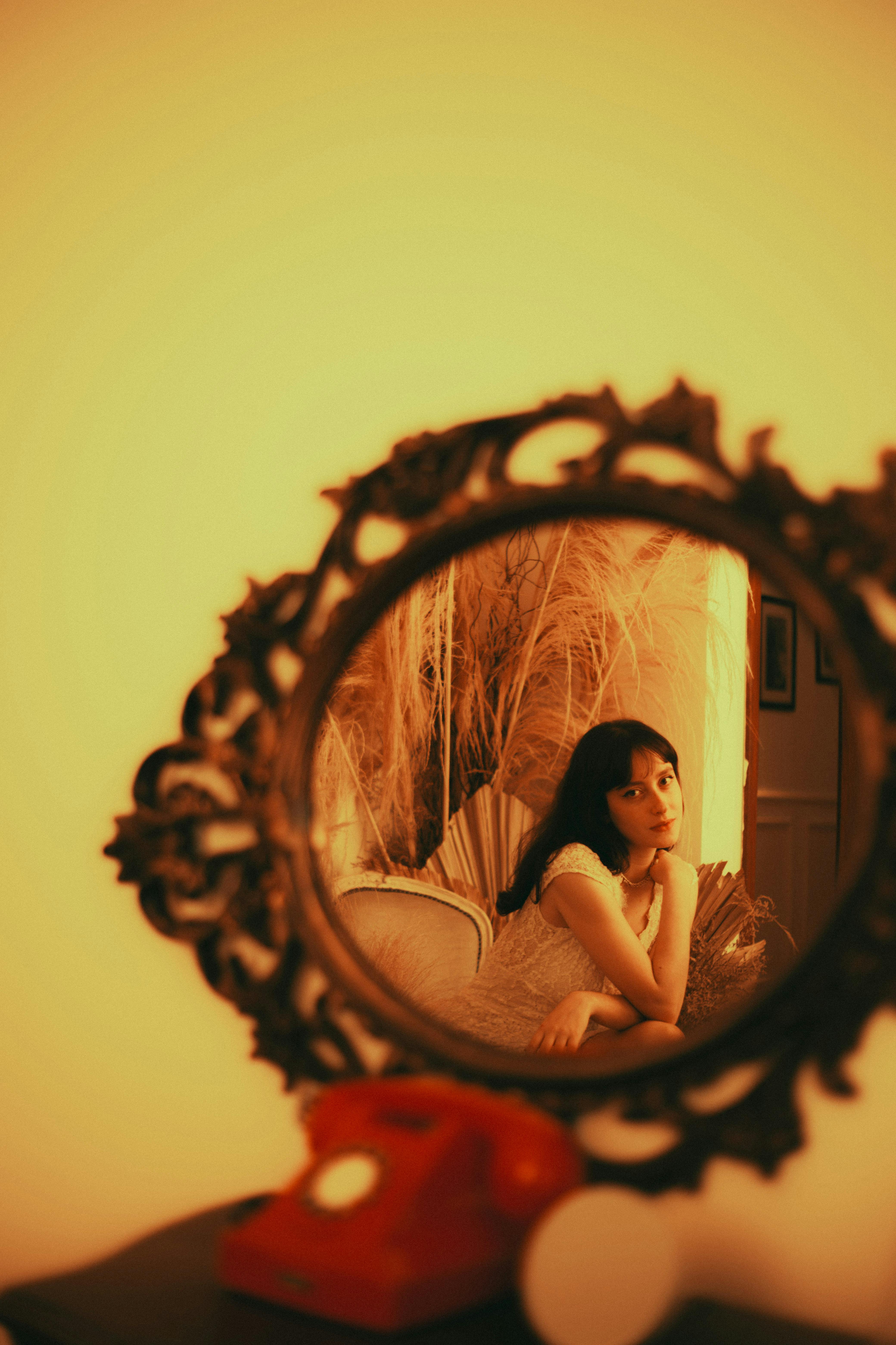Portrait of a woman reflected in ornate mirror with warm vintage tones.