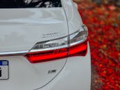 White Car with Red Taillight Near Autumn Leaves