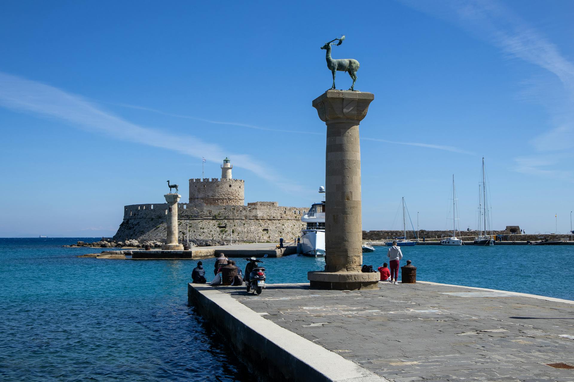 View of Mandraki Harbor with medieval fort and deer statues in Rhodes, Greece.