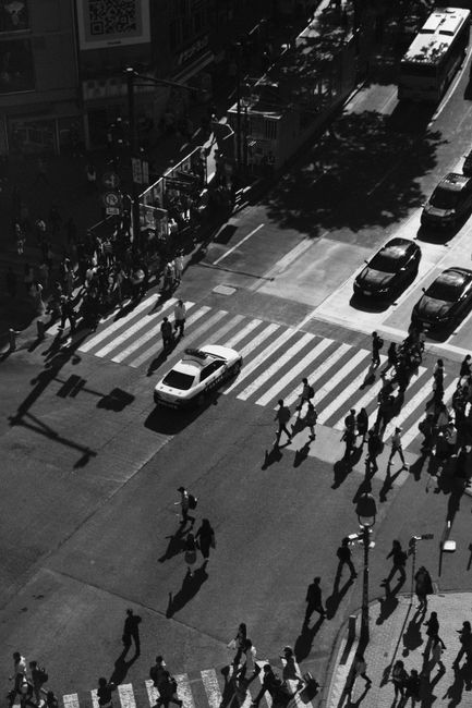 Aerial view of people crossing a busy city intersection in black and white.