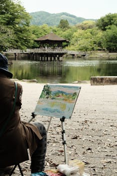 A serene scene of an artist painting by a tranquil lakeside with lush greenery.