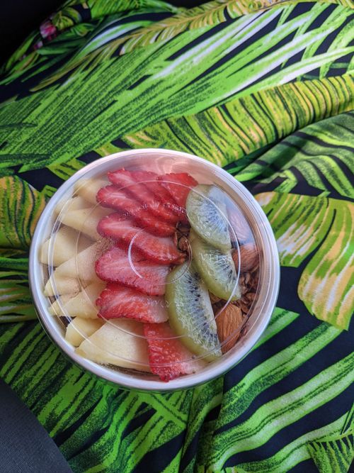 Free A delightful bowl of fresh fruit featuring strawberries, kiwi, and apples on a tropical leaf fabric. Stock Photo