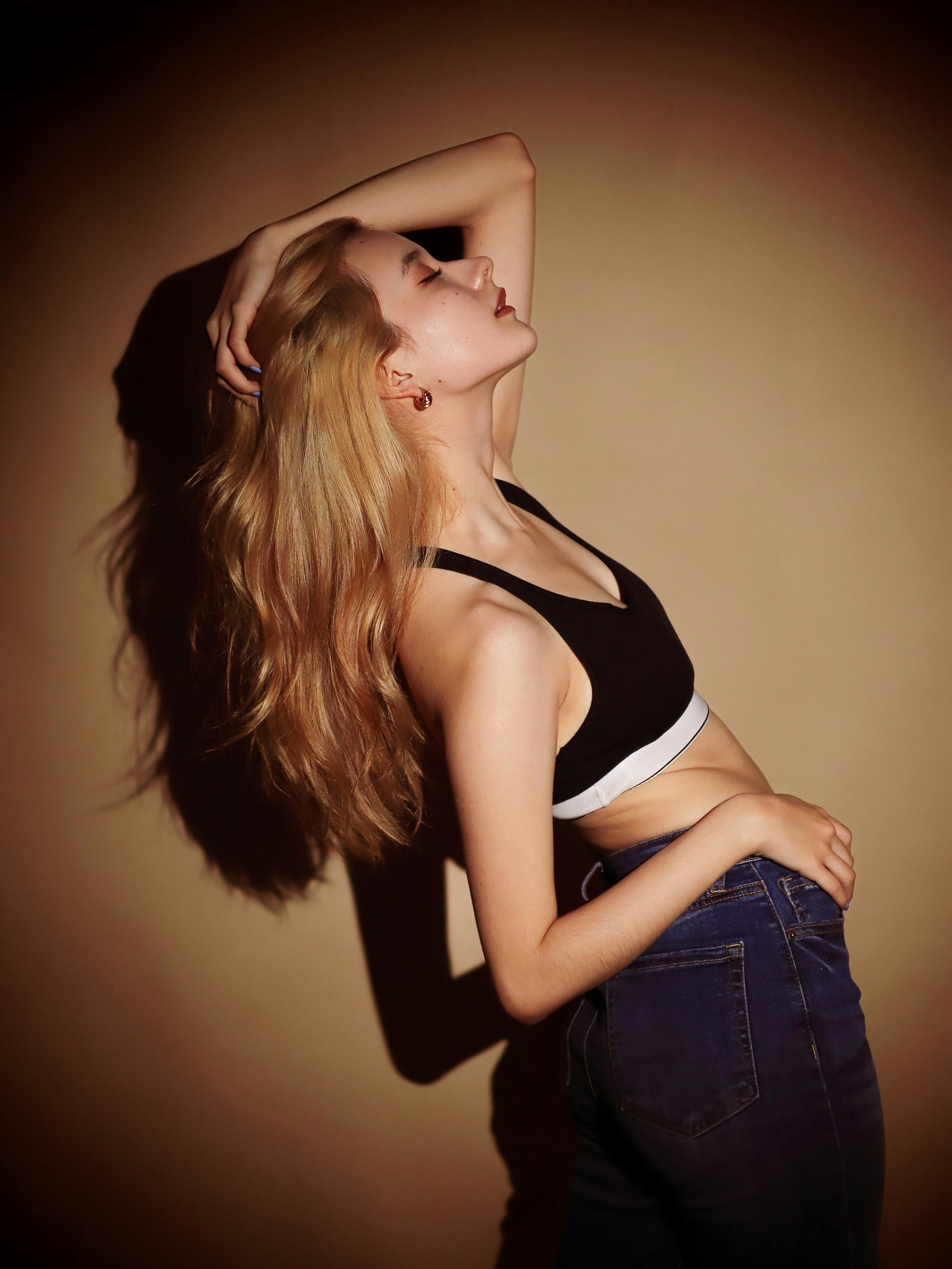 A trendy woman with long blonde hair poses in moody studio lighting, exuding elegance and confidence.