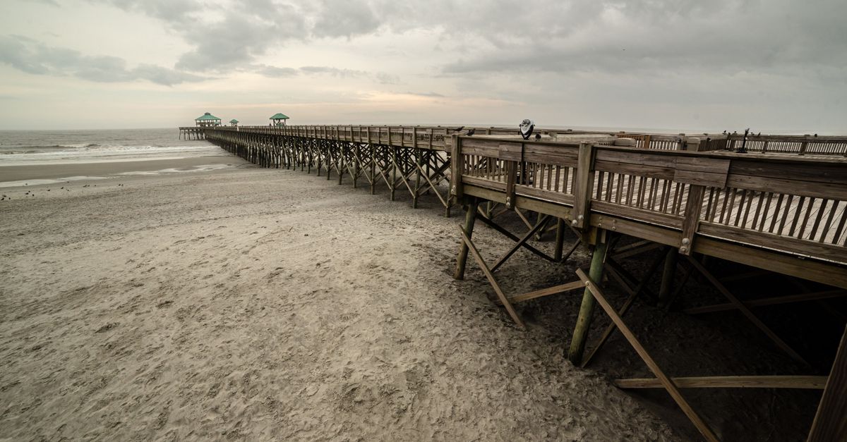 Scenic view of the wooden pier at Folly Beach, South Carolina, under a cloudy sky.