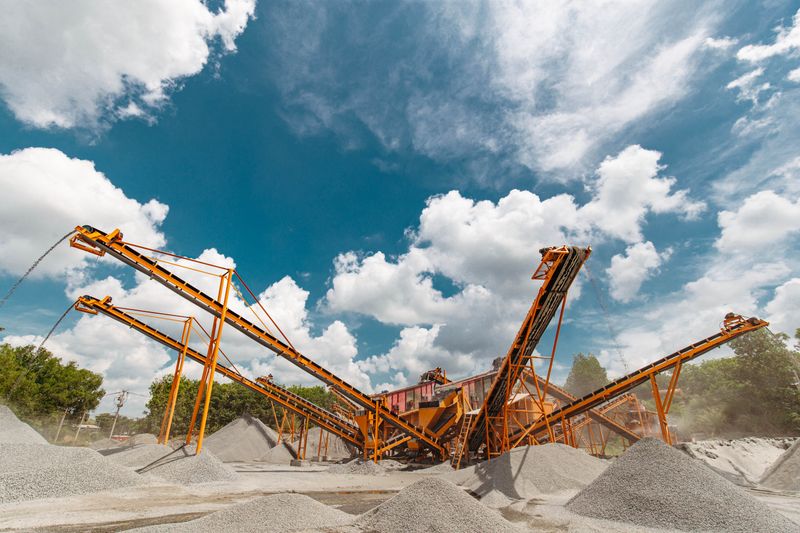 Vibrant conveyor belts moving gravel under a clear blue sky in an industrial quarry setting