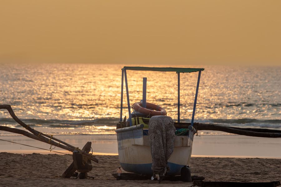 A tranquil scene of a fishing boat on the sandy beach with the golden sunset reflecting on the sea.