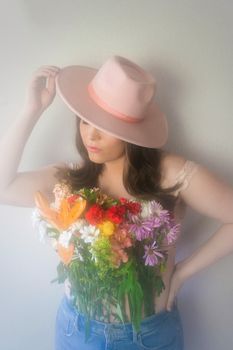 Creative portrait of a young woman in pink hat and floral arrangement, embodying a vintage aesthetic.