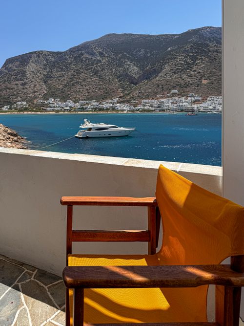 Free Relaxing view of a yacht on the Greek island coast with a vibrant yellow chair in the foreground. Stock Photo