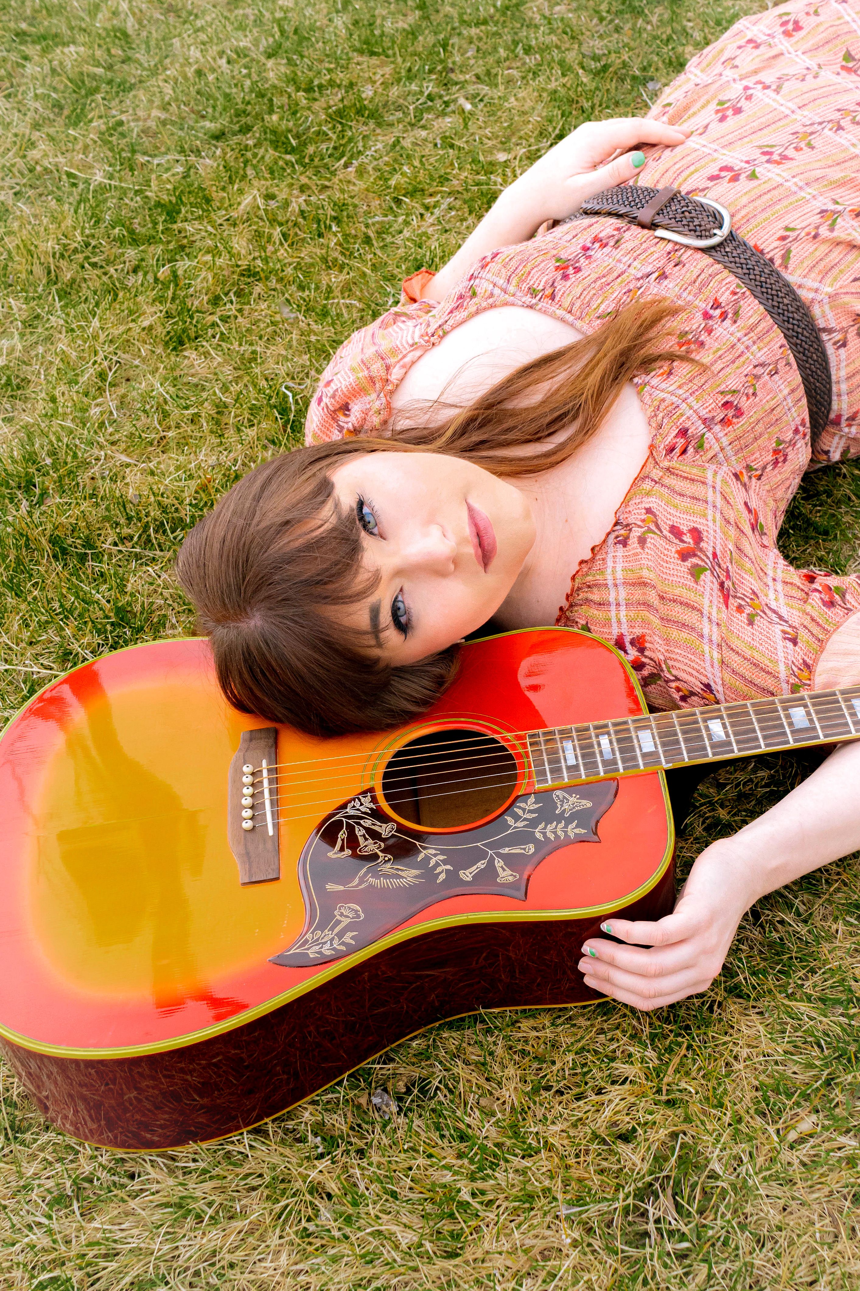 Portrait of a woman lying with an acoustic guitar on grass, evoking a vintage and musical feel.