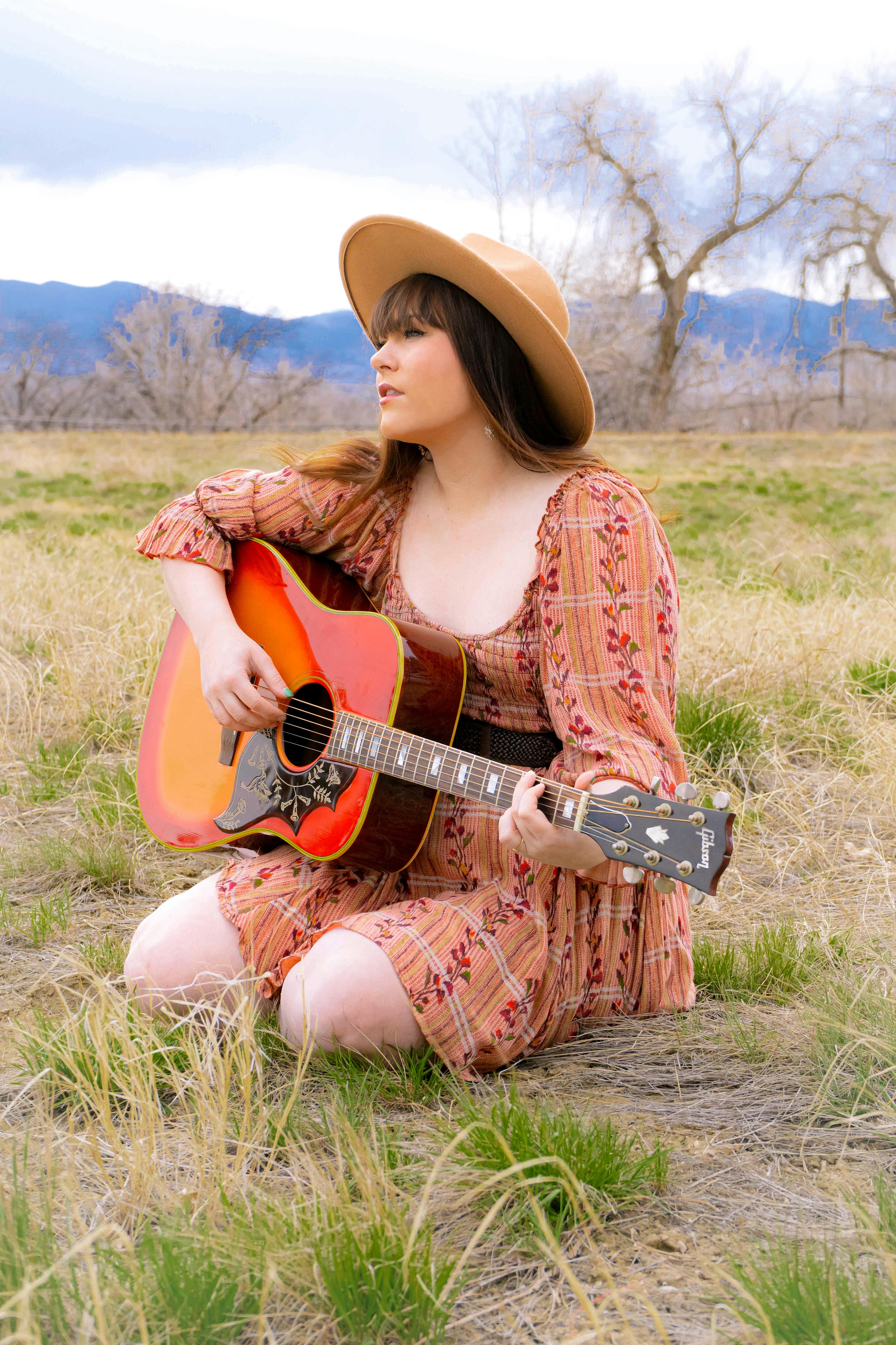 A woman in vintage attire plays an acoustic guitar in a pastoral setting. Perfect for music and lifestyle themes.