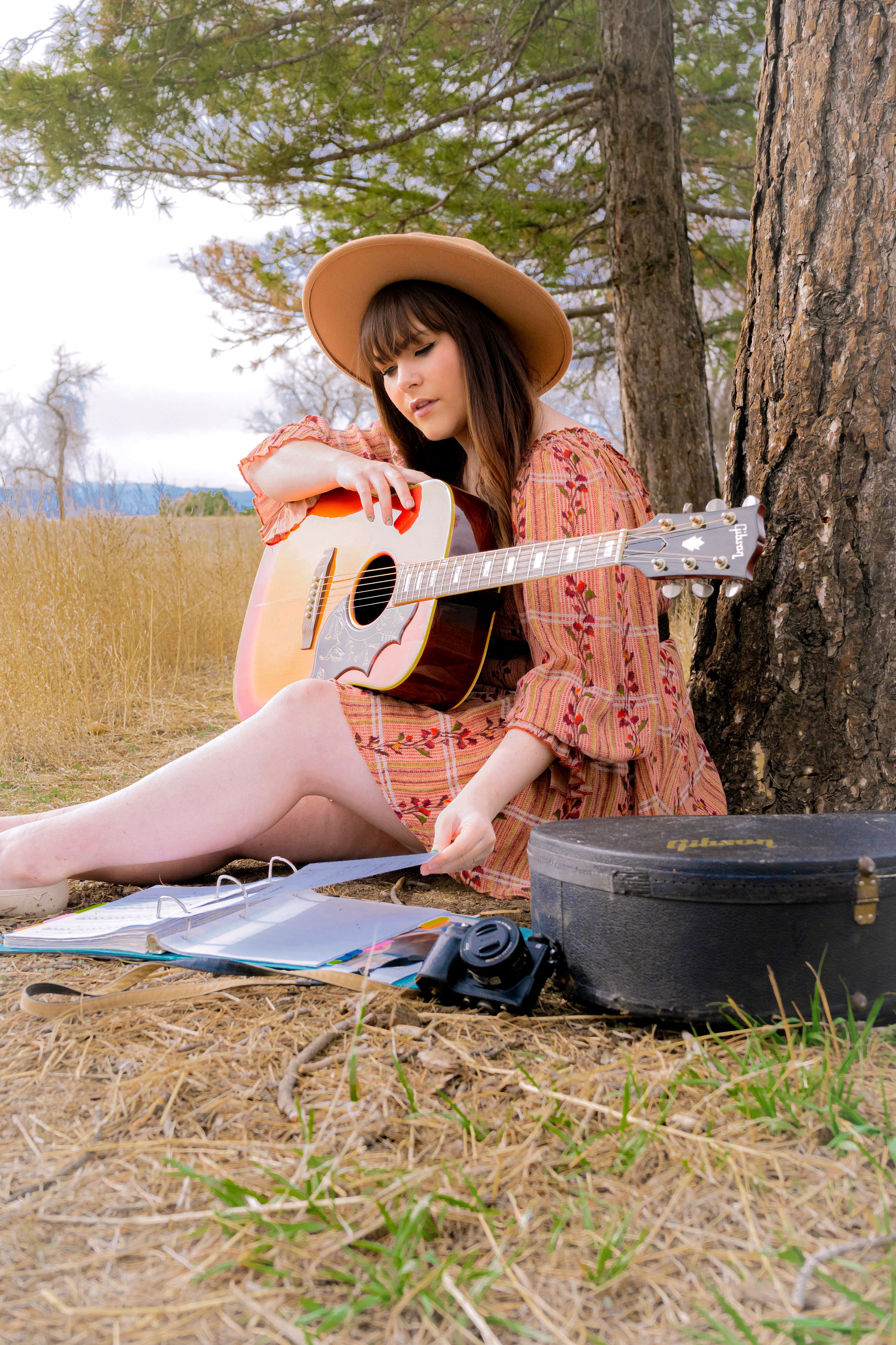 A woman plays an acoustic guitar outdoors, embodying bohemian fashion and a vintage vibe.