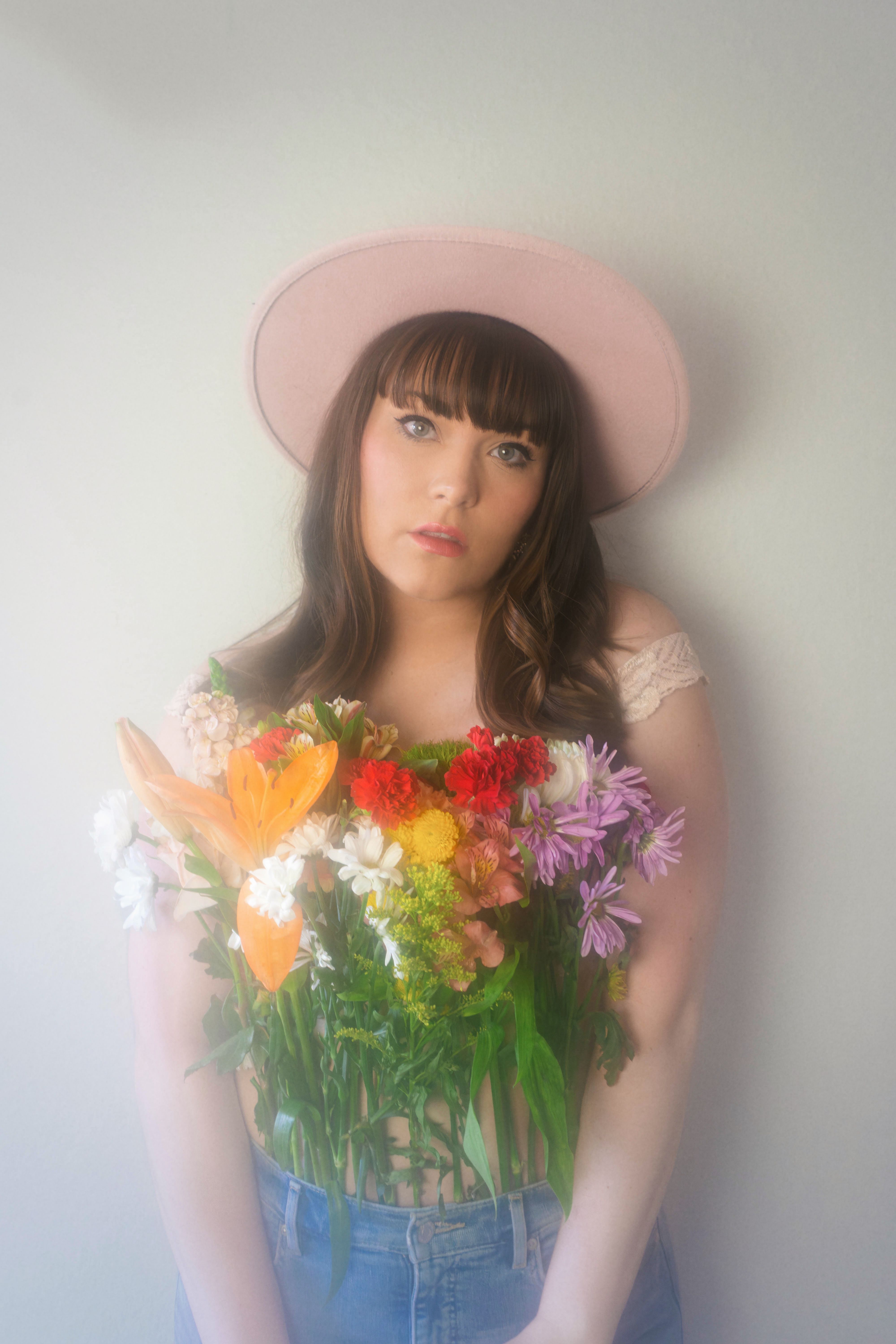A young woman in a pastel hat holding a colorful bouquet of flowers, exuding a vintage aesthetic.