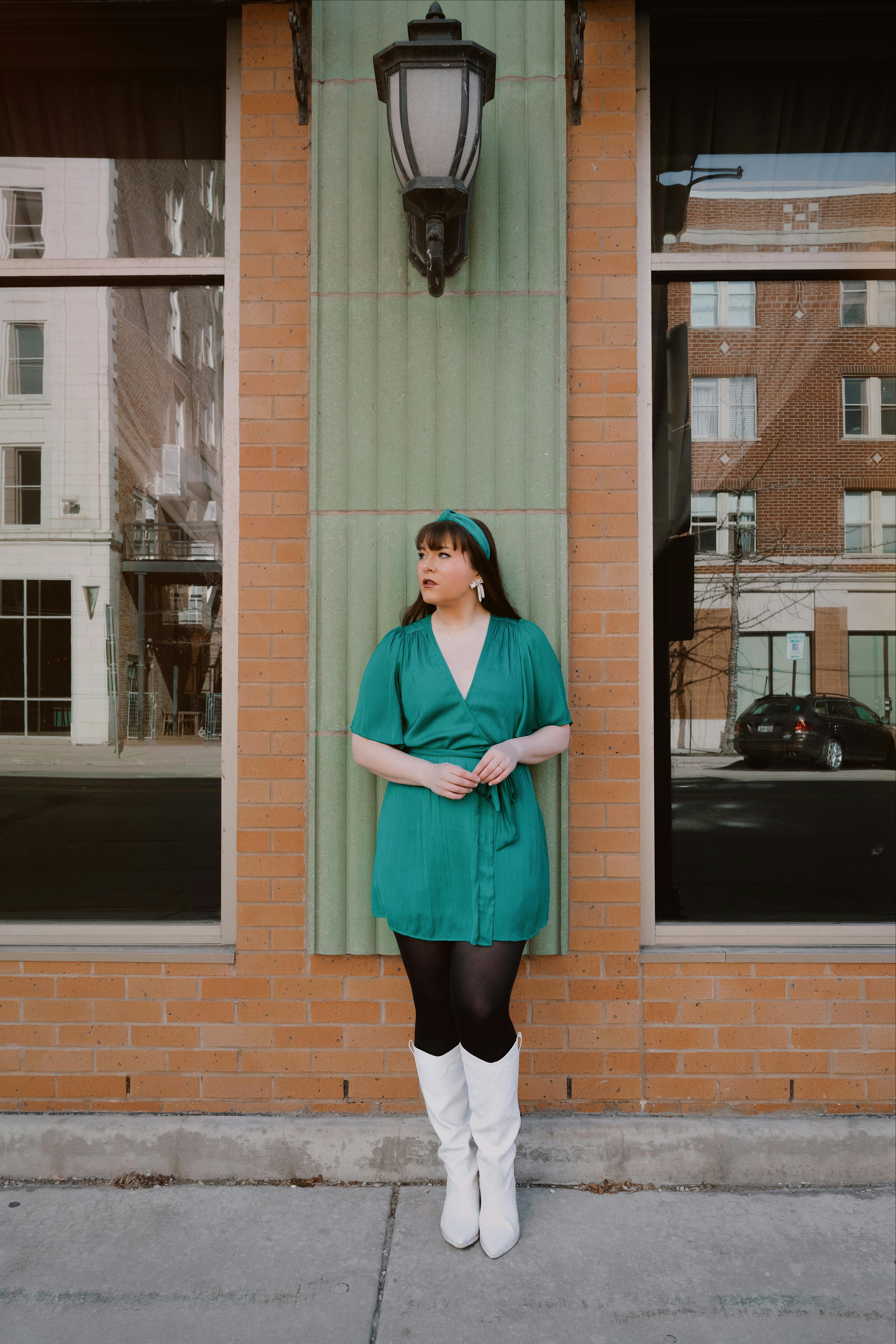 Woman in green dress and white boots standing on a city street in Wisconsin. Fashionable and retro vibes.