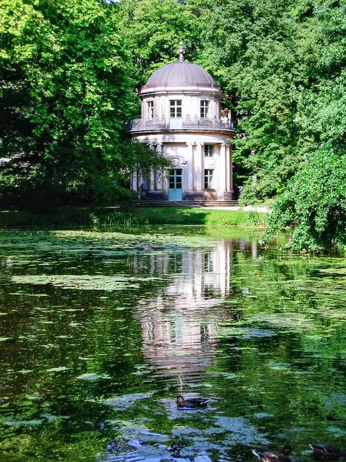 Free A beautiful round pavilion in a lush German park reflects in a tranquil pond surrounded by greenery. Stock Photo