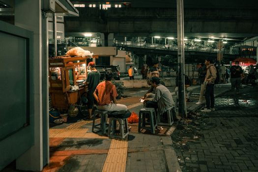 A bustling street food vendor at night with people gathered, in an urban setting.