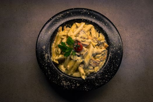 Delicious creamy mushroom pasta in a dark bowl, garnished with parsley and cherry tomato.