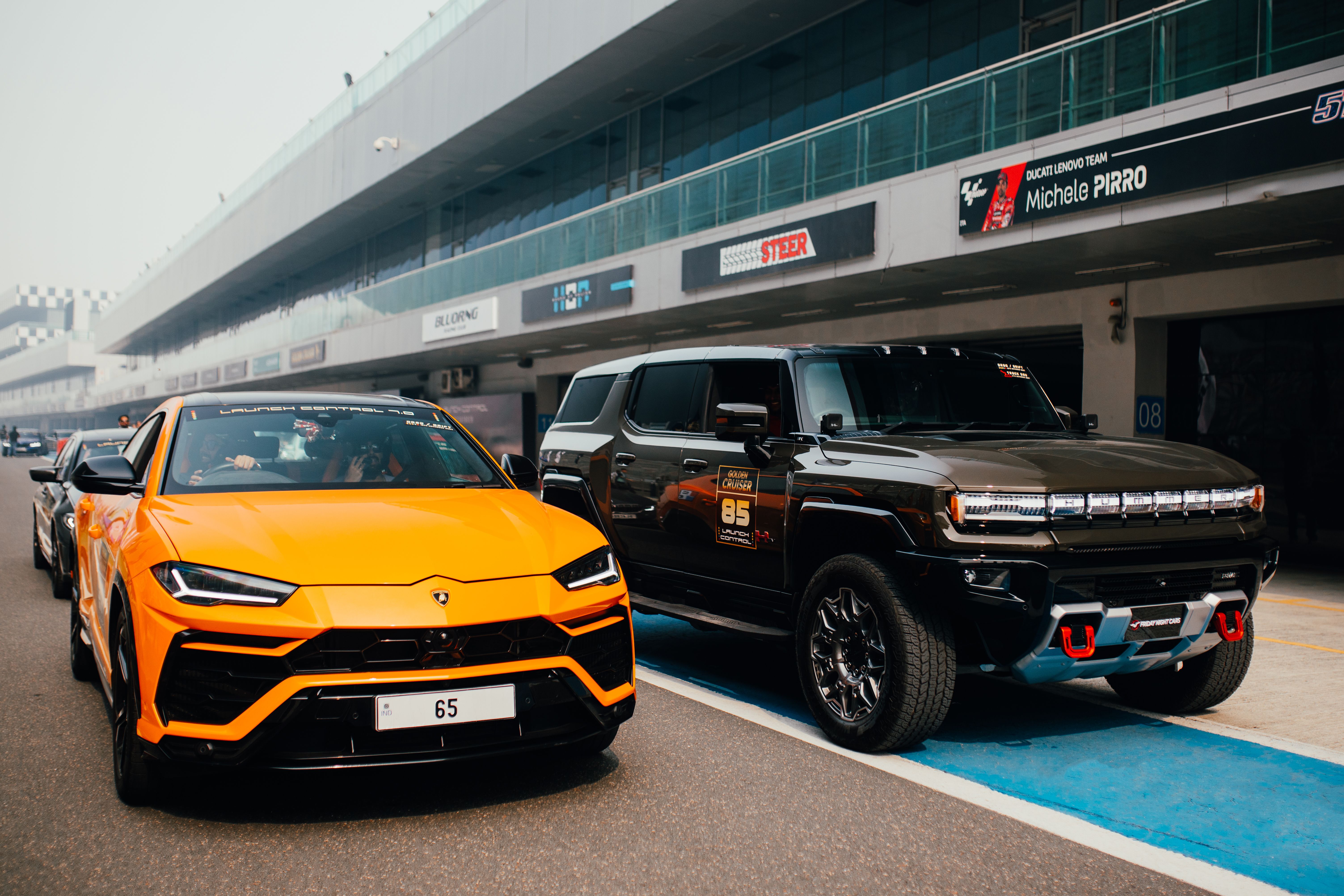 Orange Lamborghini and Black SUV parked on racetrack in Greater Noida, India.