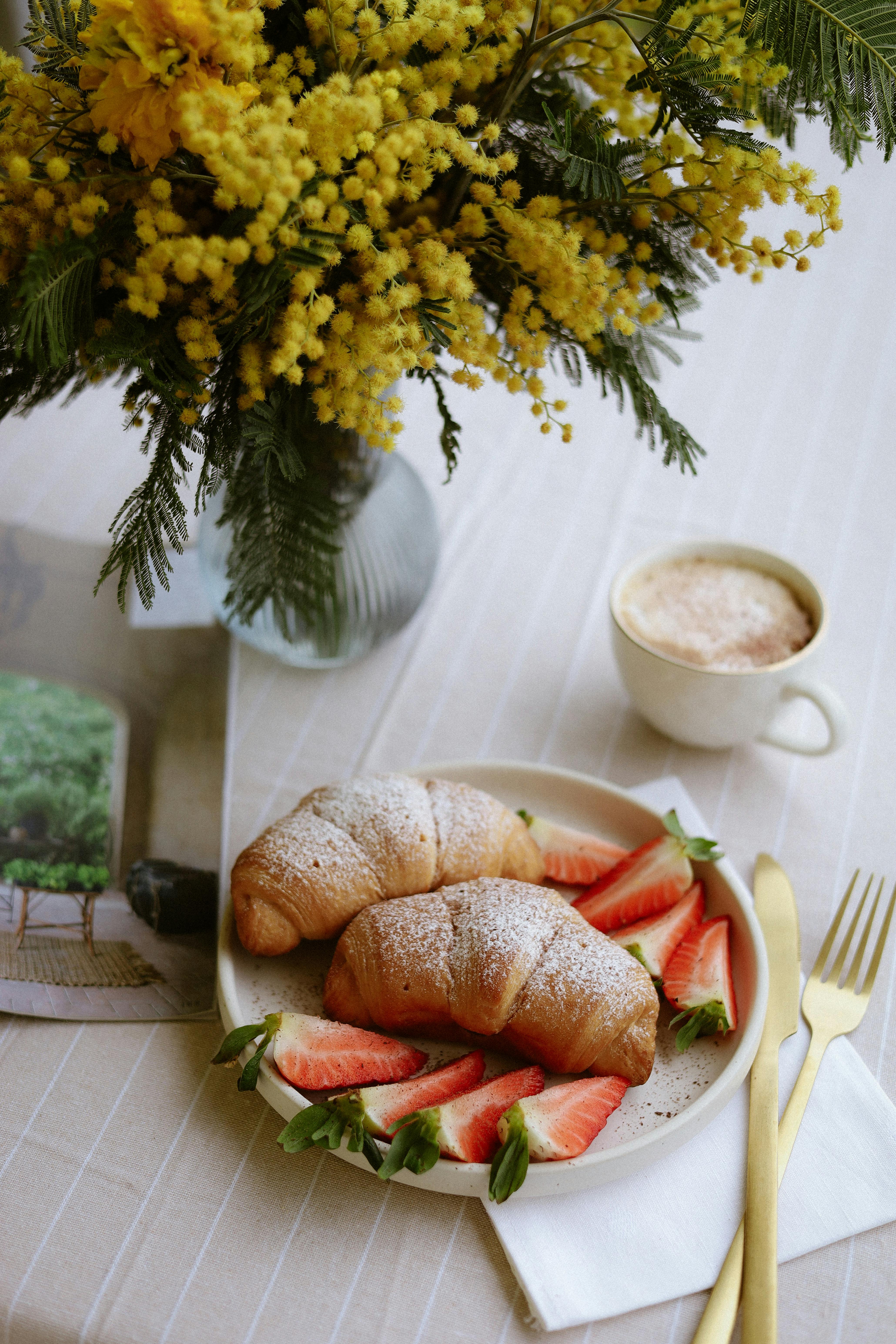 Elegant breakfast setup with croissants, strawberries, cappuccino, and floral decor.