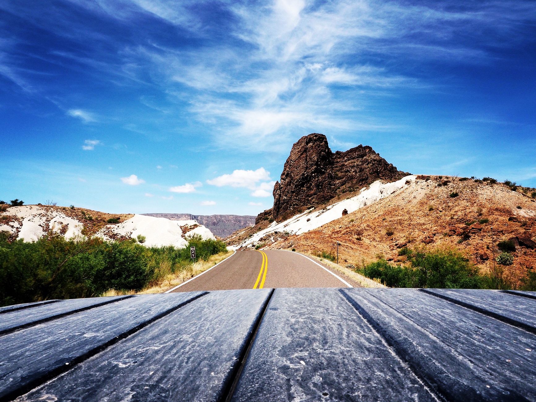 A panoramic shot of a deserted highway winding through arid hills under a vibrant blue sky.