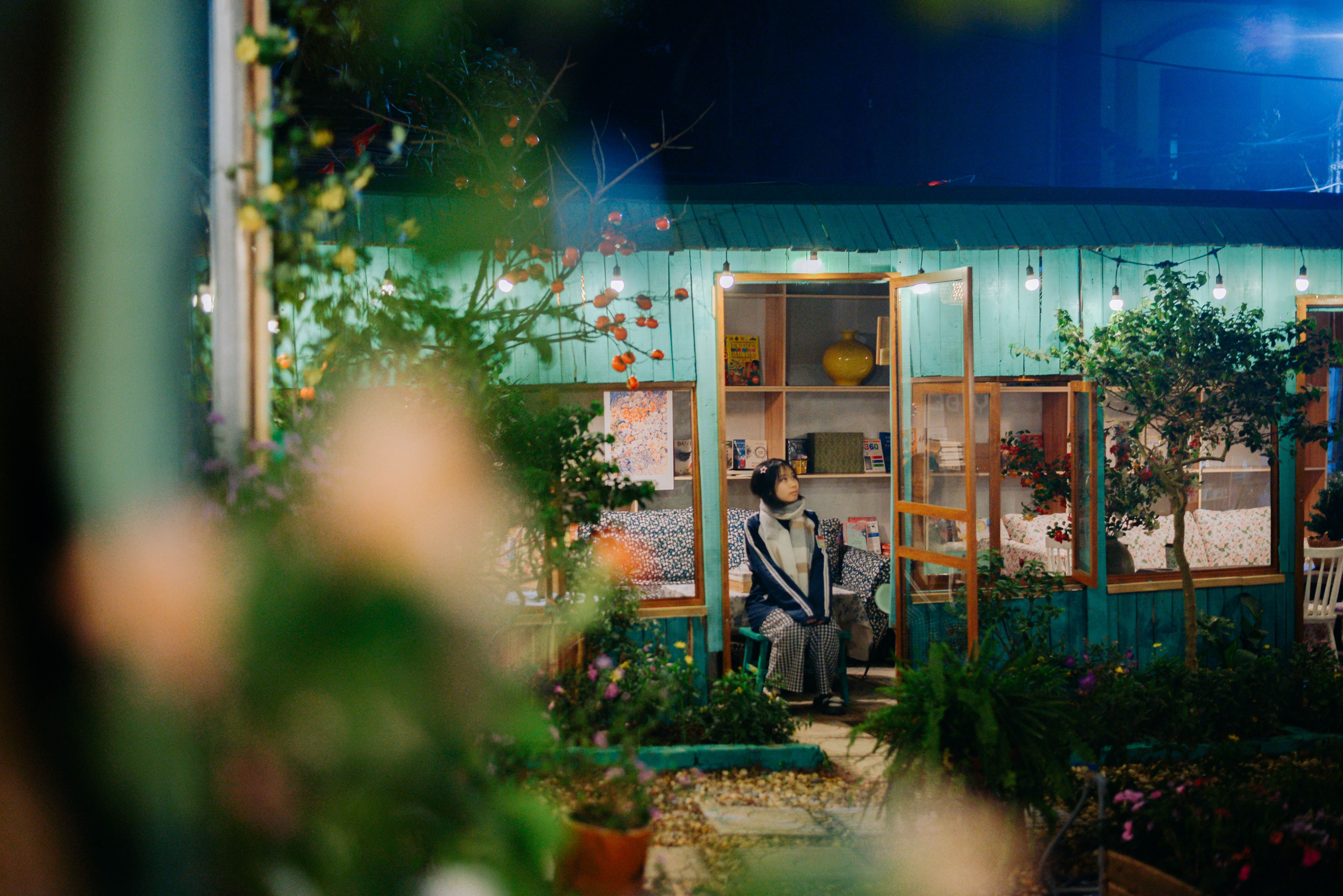 Woman sitting at a quaint outdoor café illuminated by string lights at night.