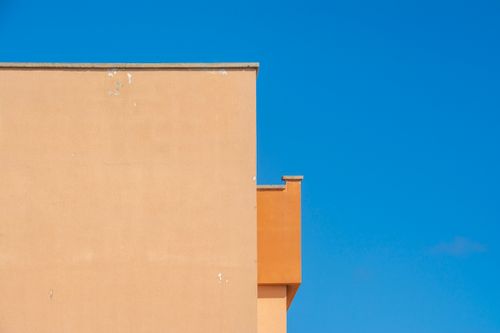 Free A minimalist shot of an orange building facade contrasting with a clear blue sky. Stock Photo