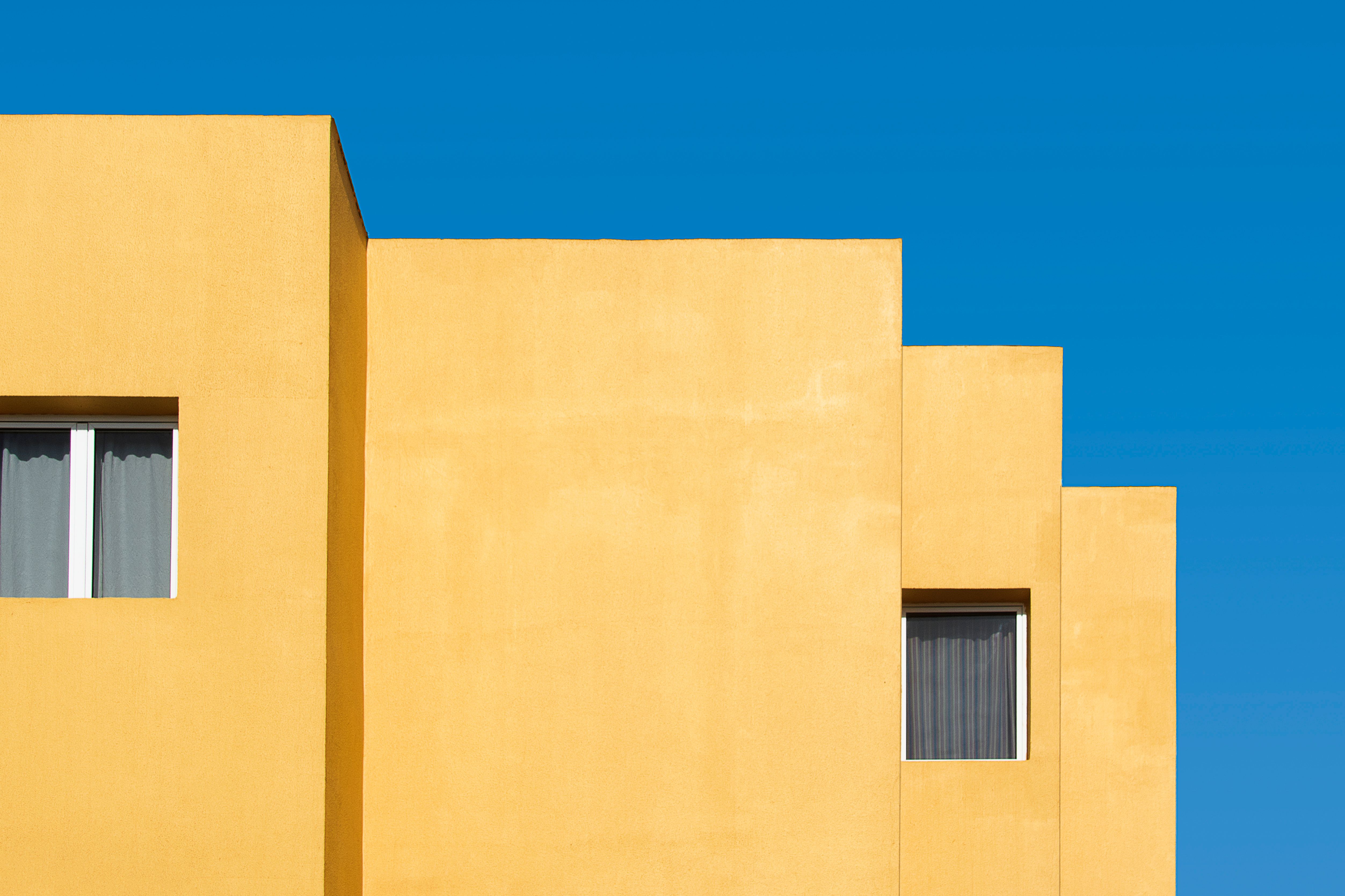 Minimalist yellow building facade with windows against a vivid blue sky.