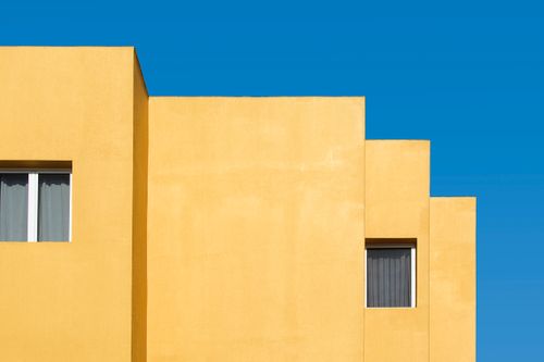 Free Minimalist yellow building facade with windows against a vivid blue sky. Stock Photo