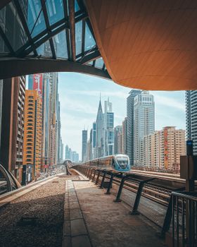 A sleek metro train glides through the vibrant cityscape of downtown Dubai, surrounded by skyscrapers.