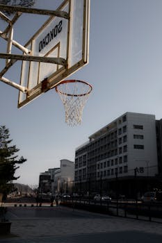An outdoor basketball hoop in a city with modern buildings in the background.