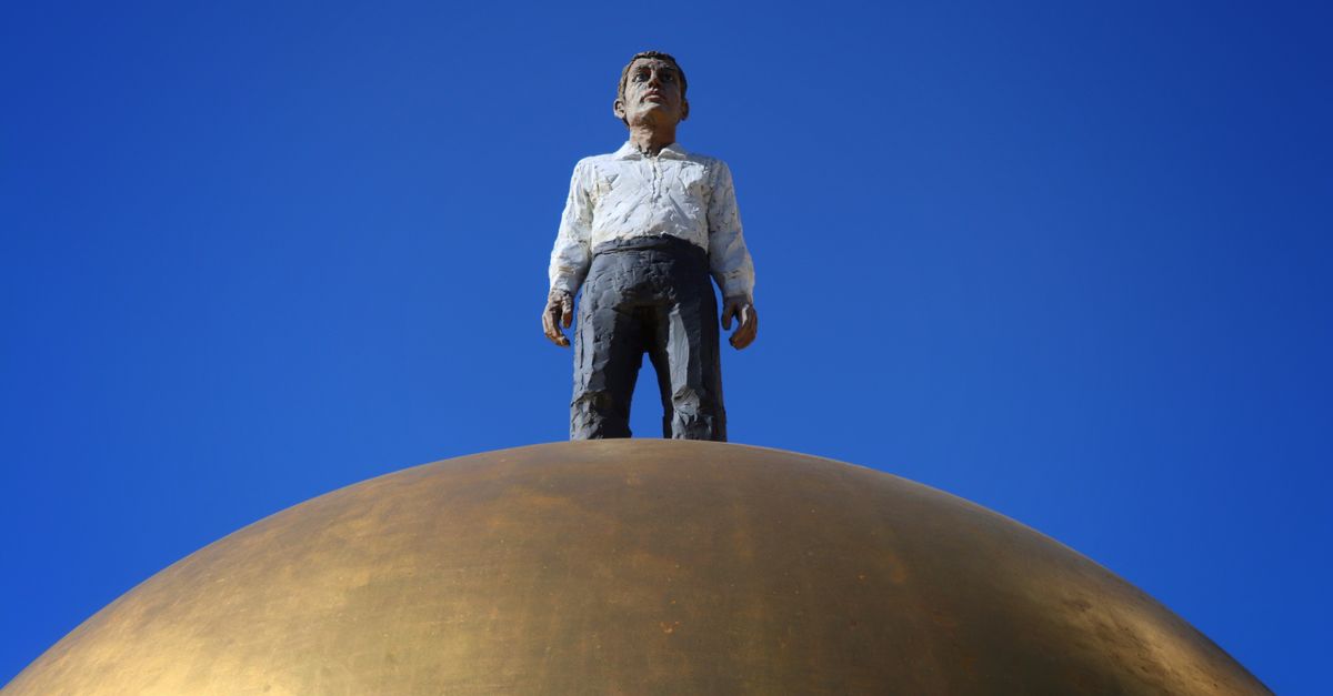 Sculpture of a man standing atop a golden globe with a clear blue sky.