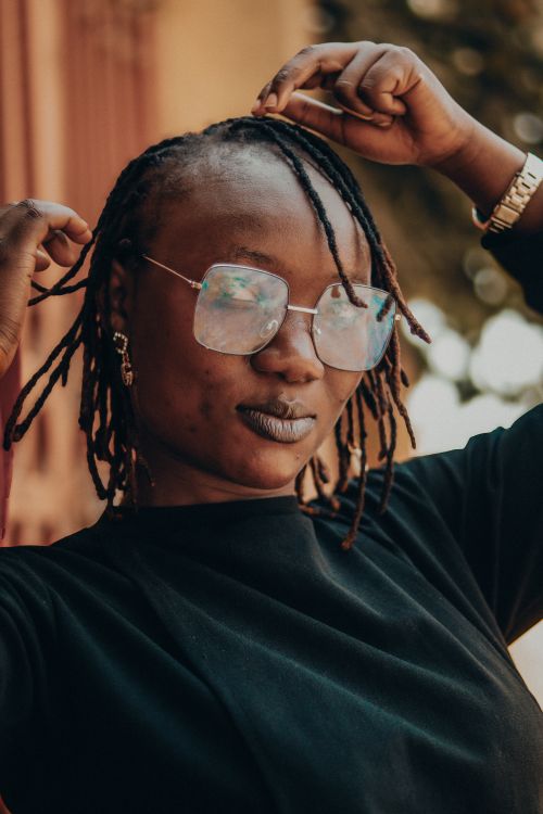 Free Portrait of a fashionable woman with dreadlocks and glasses posing outdoors in sunlight. Stock Photo