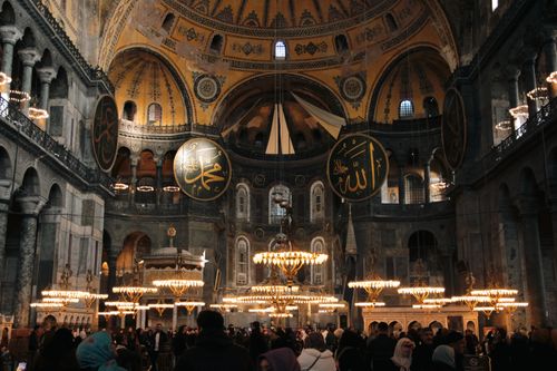 Free A bustling crowd inside the historic Hagia Sophia with ornate chandeliers and domed ceiling. Stock Photo