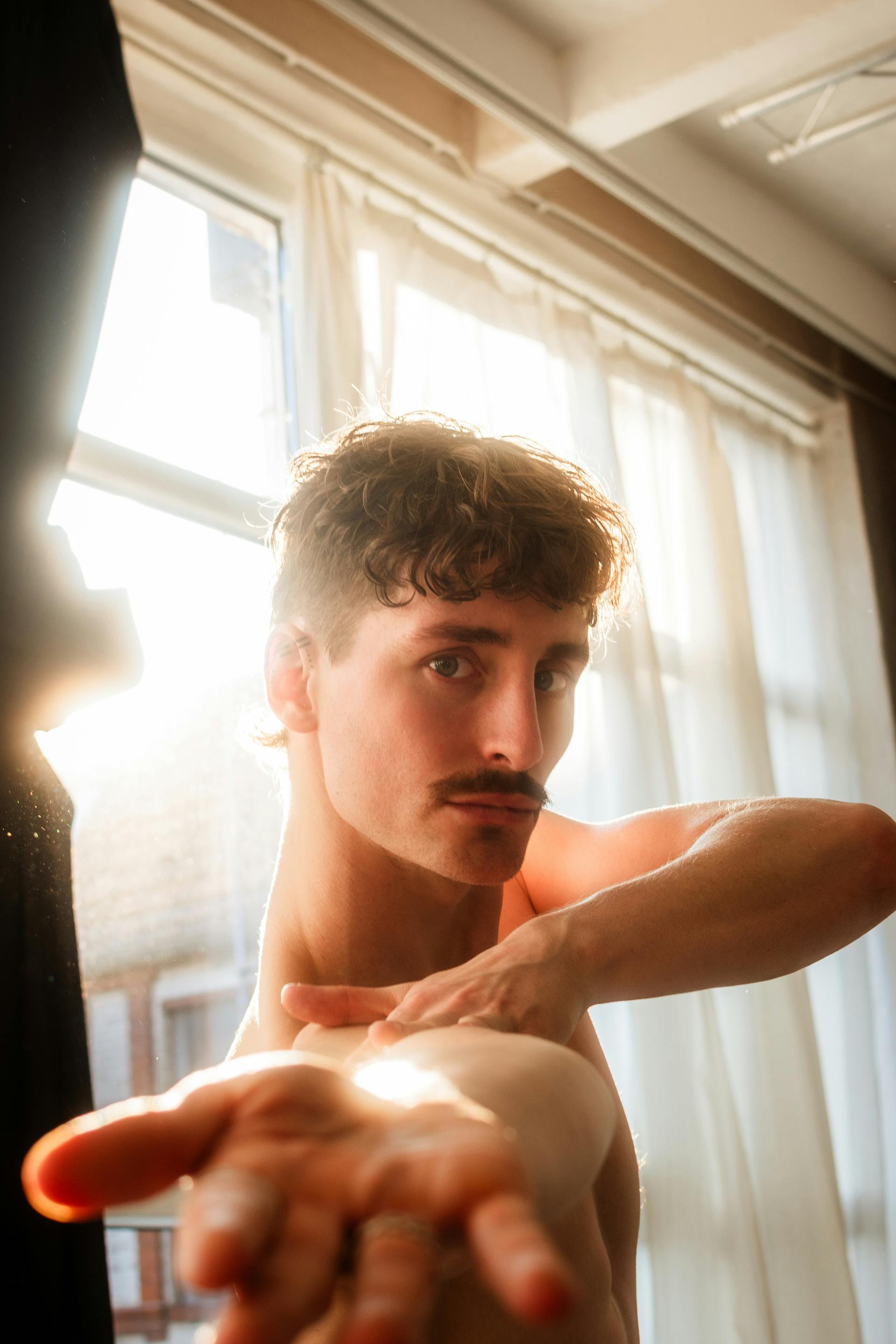 Artistic pose of a male dancer in a sunlit studio, capturing warm light and intense expression.