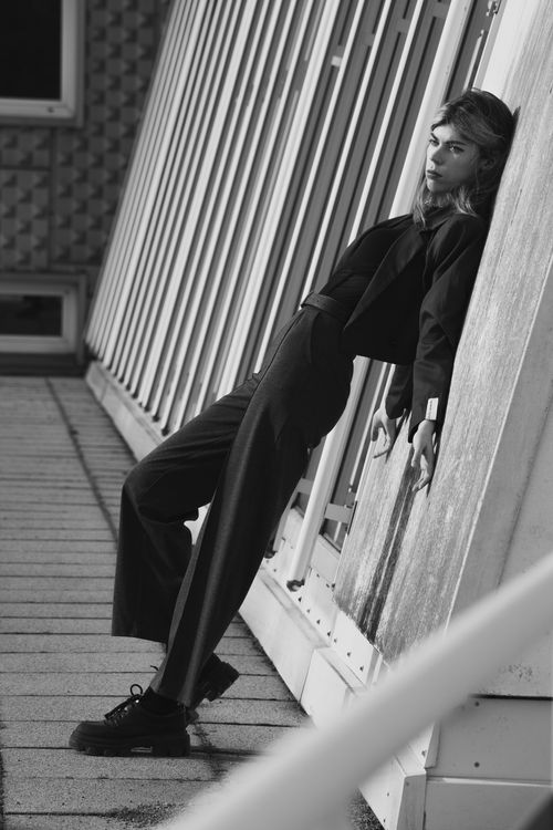 Free Black and white photo of a stylish woman posing against a building facade. Stock Photo