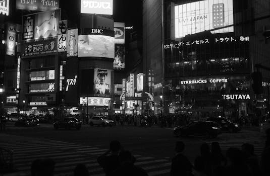 Black and white photograph capturing the bustling night scene at Shibuya Crossing, Tokyo.