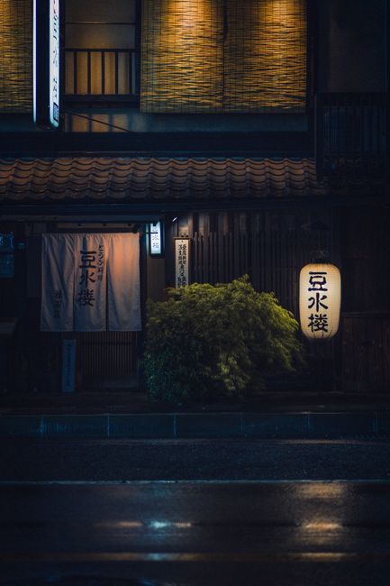 A serene nighttime view of a traditional shopfront in Kyoto, Japan, featuring lanterns.