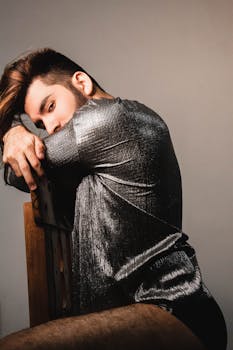 一位时尚男士身着金属衬衫，在室内椅子上摆出时尚姿势，展现现代潮流