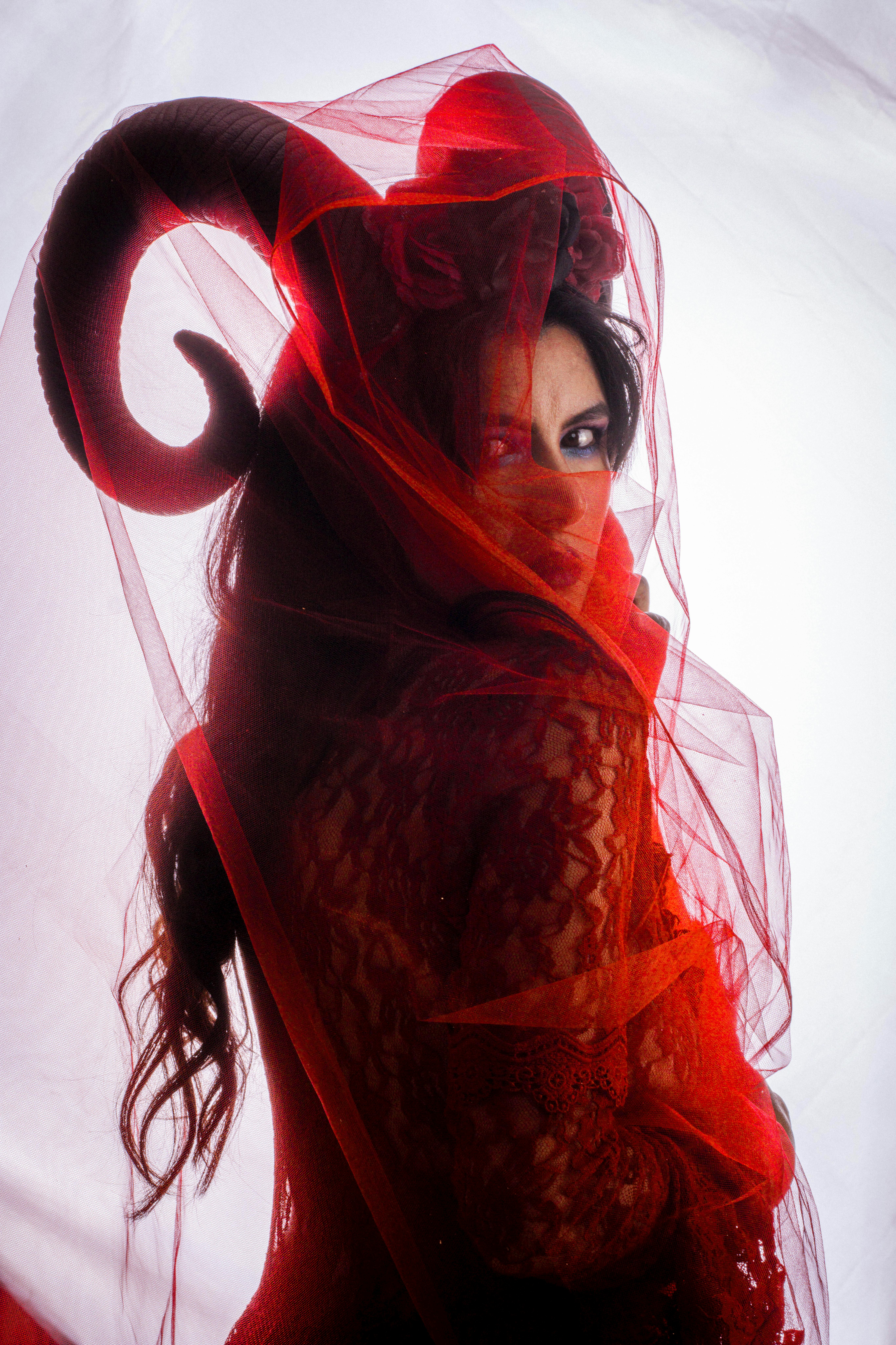 Captivating portrait of a woman in a red veil with horned costume, exuding mystery.