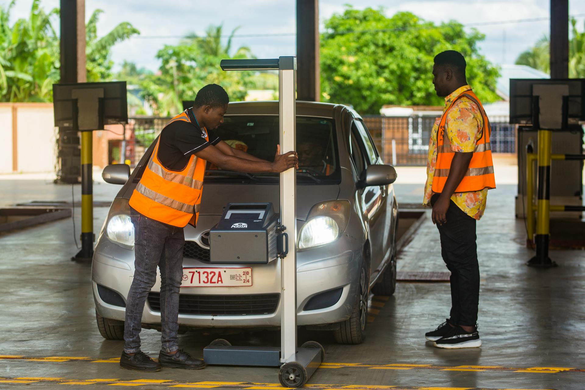 Two workers perform a detailed inspection on a car inside a garage, ensuring safety and compliance.
