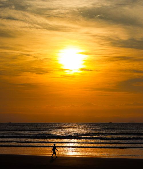 Free A child walks along the beach at sunset, creating a serene and picturesque scene. Stock Photo