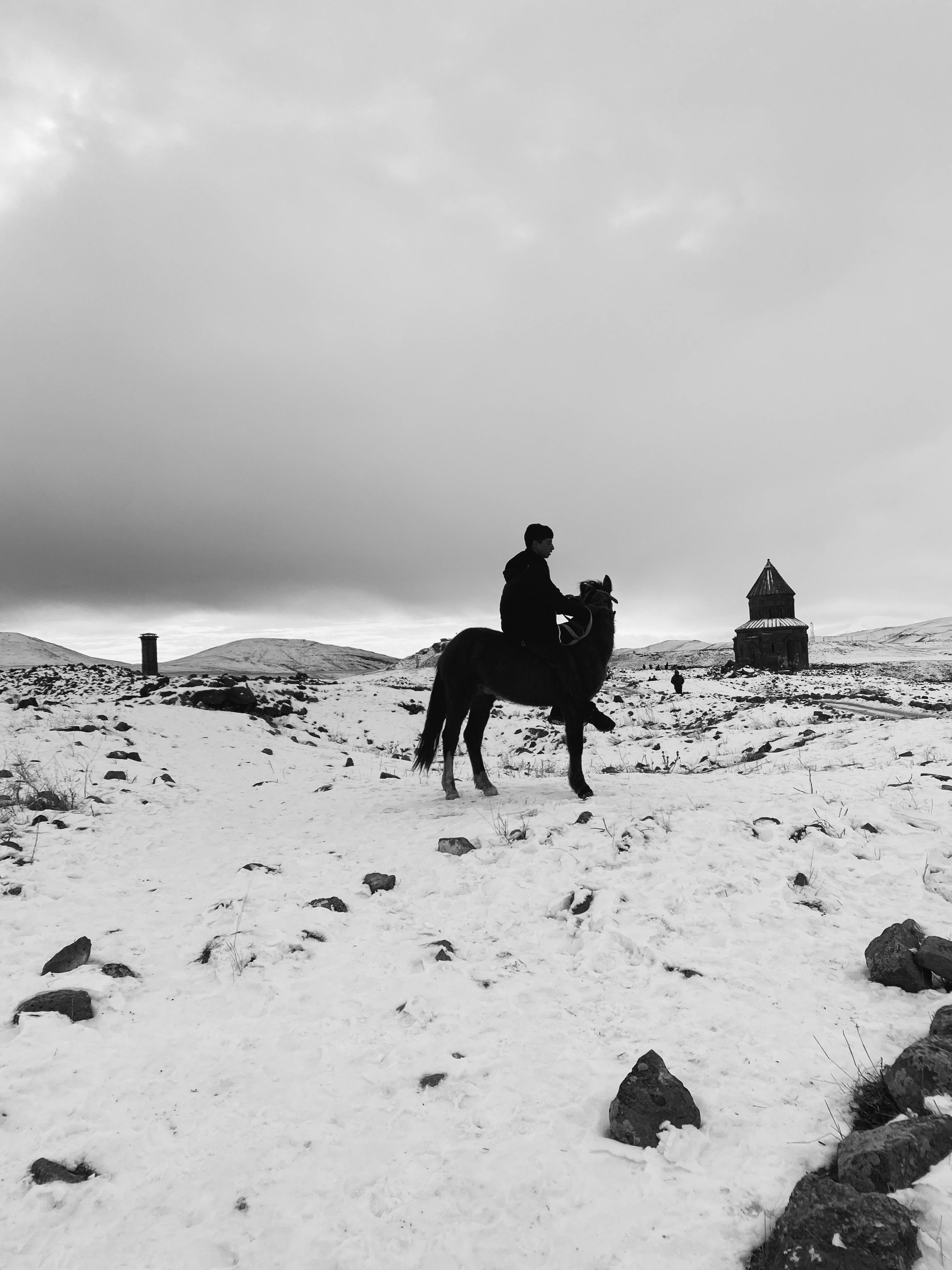 Silhouette of a horseman in a snowy Armenian landscape with an ancient church in the background.
