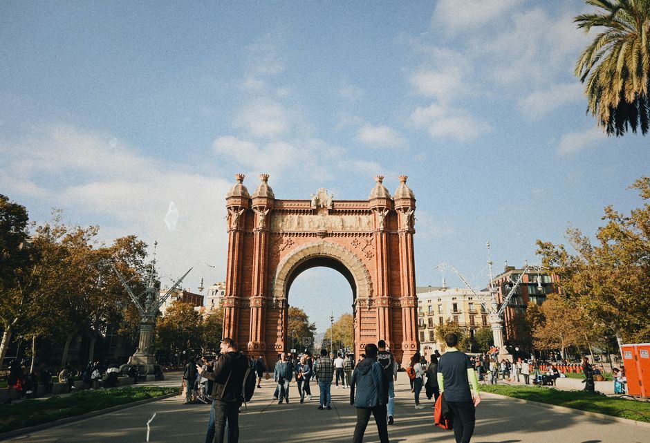 Personas caminando cerca del Arco de Triunfo en Barcelona con cielos despejados sobre ellos.