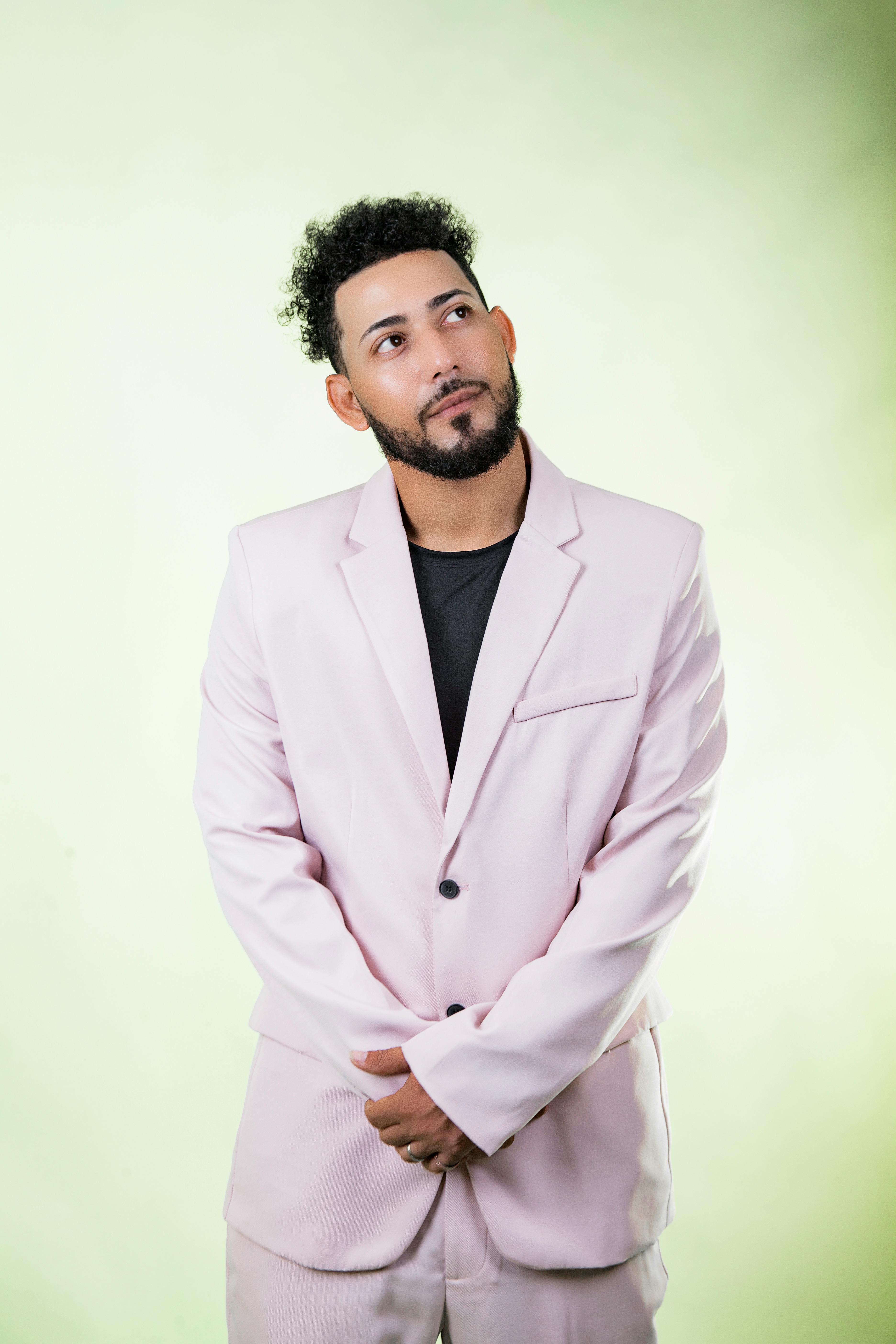 Young man in pink suit looking thoughtful against green backdrop.