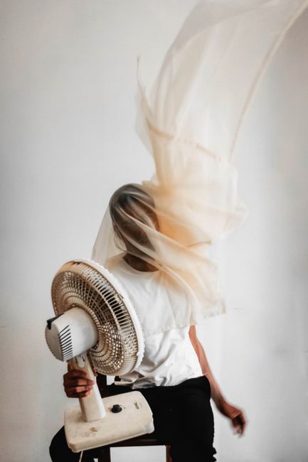 Abstract portrait of a person with a fan and flowing fabric, capturing motion indoors.